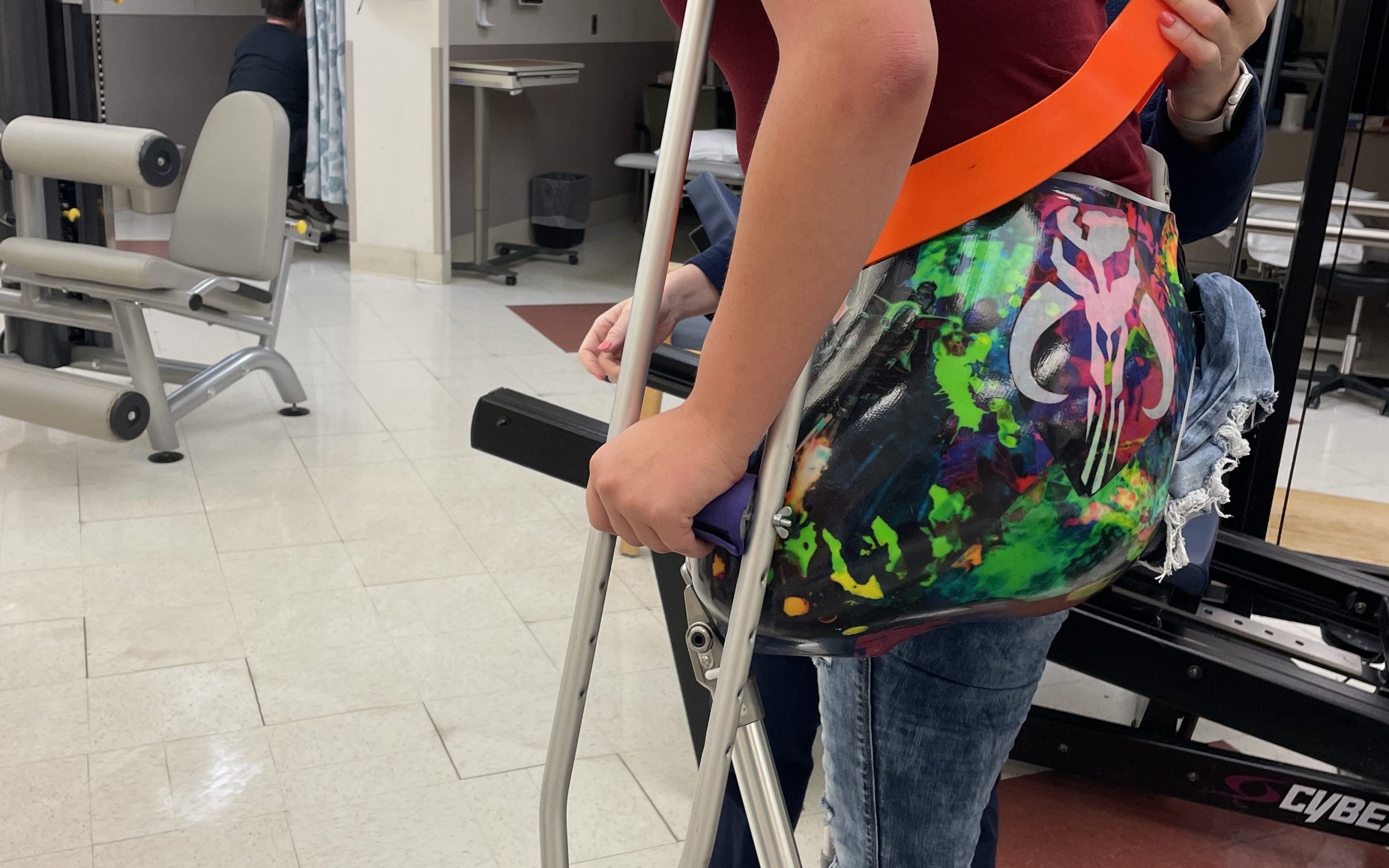 My daughter preparing to take a step in her new prosthetic. She has under arm crutches and there is a bright orange gait belt around her waist.