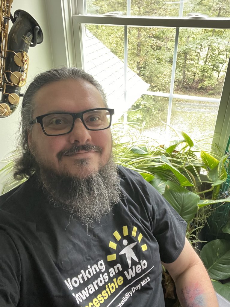 Nick sitting in his office wearing a shirt that says, "Working towards and accessible web. WP Accessibility Day 2023"